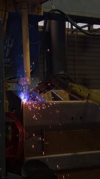 No people vertical shot of welding robot assembling heavy machinery and producing blue sparks, modern computer-aided technologies at manufacturing factory