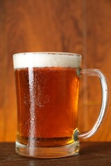 Mug with fresh beer on wooden table against color background, closeup