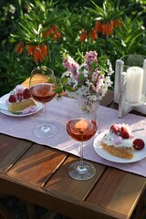 Vase with spring flowers, wine and cake on table served for romantic date in garden
