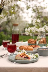 Stylish table setting with beautiful spring flowers, fruit drink and pie in garden