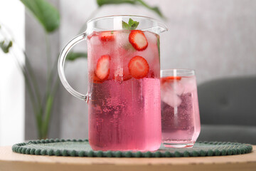 Freshly made strawberry lemonade with mint in jug and glass on wooden table indoors
