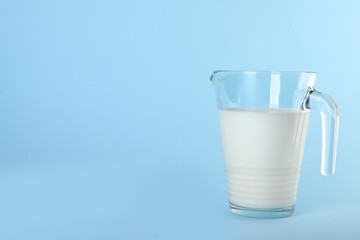 Jug of fresh milk on light blue background, space for text