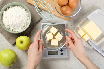 Woman weighing butter on kitchen scale at grey table, top view
