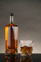 Bottle and glass with whiskey on table against gray background