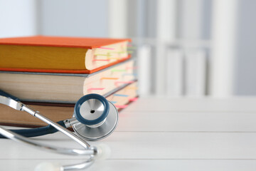 One new medical stethoscope and books on wooden table, closeup. Space for text