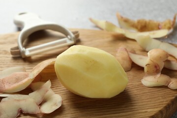 Fresh raw potato, peels and peeler on table, closeup