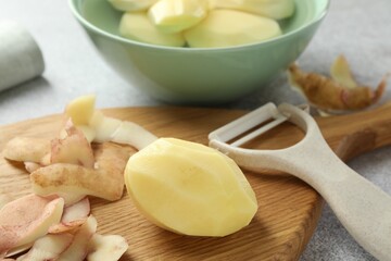Fresh raw potatoes, peels and peeler on light grey table
