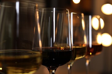 Different tasty wines in glasses against blurred lights, closeup