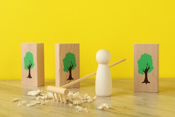 Wooden human figure with rake and sawdust among planks with drawn trees on table against yellow...