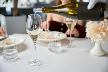 Close up of hand of waiter in gloves pouring white wine into glass for couple in the restaurant