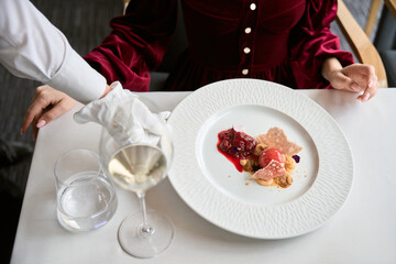 Top view of waiter hand in white gloves putting plate with tasty food for lady in the restaurant