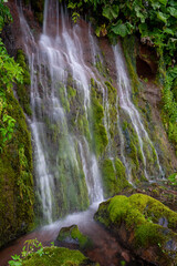 A wall of waterfalls on a green moss-covered slope of a volcano, Iturup Island