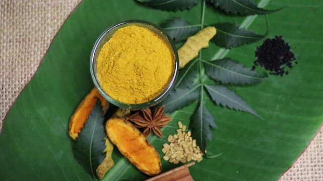 Close up slow motion footage of turmeric root,  turmeric powder, neem, black cumin, anise in banana leaf background as ayurvedic concept. Traditional herbal treatment ingredients and herbs
