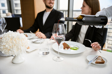 Happy couple talking and sitting in restaurant, while waiter pouring wine