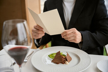 Cropped photo of man in black suit holding bill while sitting in the restaurant