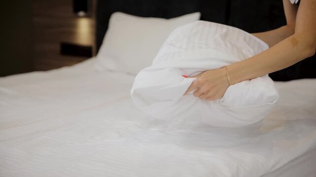 Hotel cleaning concept. Close-up of young maid in uniform making bed in room, fluffing pillows and punching them into shape. Preparing hotel room for new guests