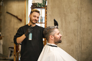 Smiling hairstylist applying cologne or fixing spray on client's haircut