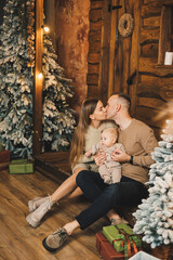 Happy family near the Christmas tree. A young father and mother hold their son in their arms and show him something. New Year in the family circle.