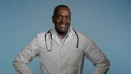 Smiling happy confident african american man professional physician male doctor successful ethnic medical worker clinic surgeon posing in studio blue background looking at camera healthcare medicine