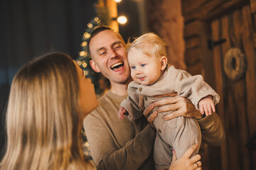 The atmosphere of the Christmas holidays. A happy family with a small child celebrates the New Year together near the Christmas tree in a cozy house. Christmas in the family circle.