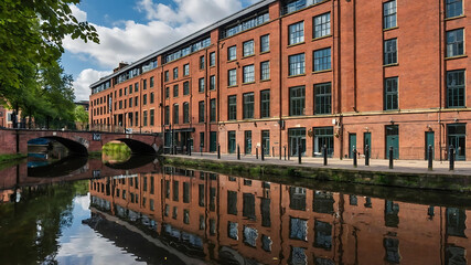 Naklejka premium Wide Shot of the Building and Canal: A wide shot of Piccadilly Village, a picturesque red brick building by the canal The building reflects in the water. The scene includes narrowboats 