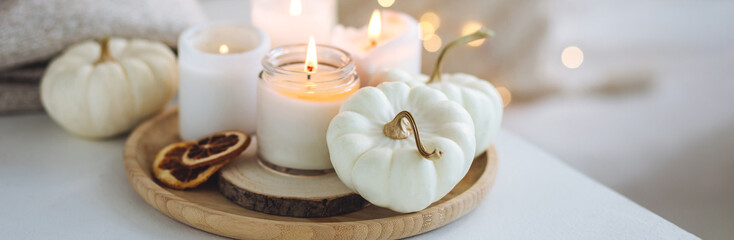 Atmospheric aroma candles with sweet spicy scent and white pumpkins on wooden tray, autumn bedroom decor. Autumn cozy home and hygge concept, place for relaxation, detention. Aromatherapy. Banner