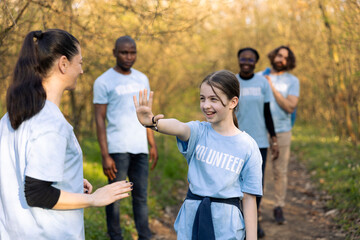 Activist congratulating a little child with a high five gesture, praising her team members after a job well one volunteering to help nature ecosystem. People showing perseverance.