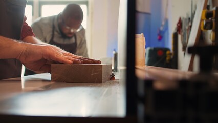 Man putting lumber block through spindle moulder, creating smooth edges on wooden piece. Joiner using heavy machinery to craft joints for furniture and structures, camera B close up