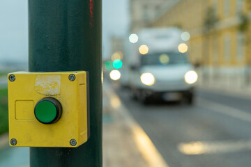 Green button with yellow frame to stop traffic on crosswalk with blurred car traffic background