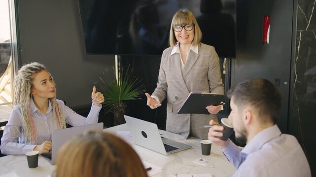 A business meeting with a presentation in a modern office, where professionals and an elderly businesswoman, the company director, participate in discussions