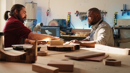 Artisan and apprentice comparing wood art piece with schematic displayed on CAD software on laptop....