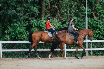 Obraz premium Two riders enjoy horseback riding in an outdoor arena. The scene is framed by lush green foliage, creating a serene atmosphere.
