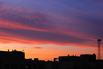 bright sunset sky over the silhouettes of city roofs, sky with changing weather