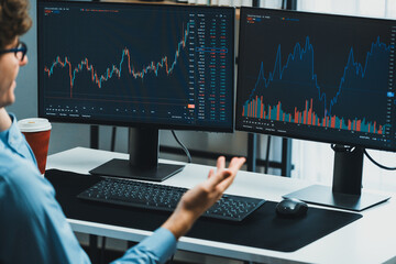 Young investor stock trader discussing on smartphone to broker, looking on dynamic financial exchange investment on screen at back side in current market graph in real time at modern office. Gusher.