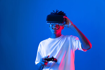 American African gaming player wearing VR controlling joystick hologram isolated blue pink neon lighting wall screen connect digital futuristic technology virtual reality metaverse world. Contrivance.