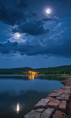 Obraz premium Full Moon Over Tranquil Lake with Rocky Shore.