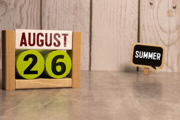 Wooden block calendar with the date August 26 and spikelets of wheat on a beige concrete background.