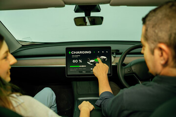 Two lovely couple inside the vehicle, checking battery recharging electricity status display on...