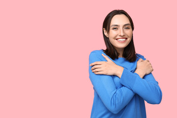 Young woman hugging herself on pink background