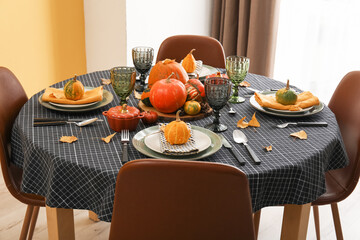 Beautiful table setting with autumn leaves and pumpkins in dining room