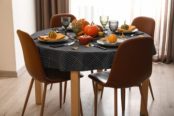 Beautiful table setting with autumn leaves and pumpkins in dining room