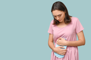 Obraz premium Young woman with hot water bottle suffering from menstrual cramps on blue background