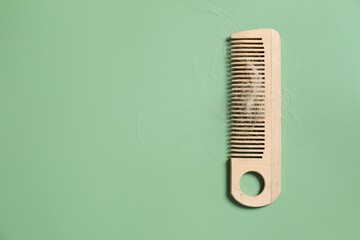 Wooden comb with lost hair on green background, top view. Space for text