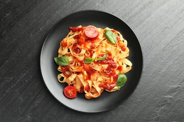 Delicious pasta with tomato sauce, vegetable and basil on dark textured table, top view
