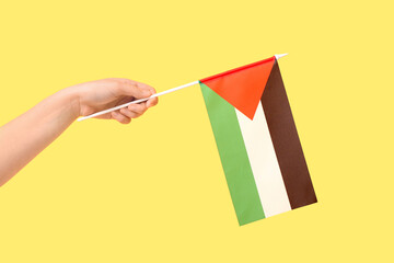 Female hand with flag of Palestine on yellow background