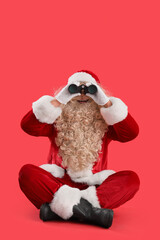 Santa Claus looking through binoculars on red background