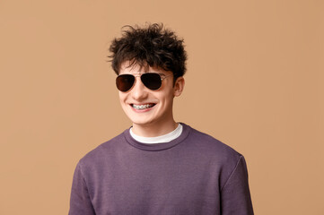 Handsome young man in stylish clothes and sunglasses on brown background