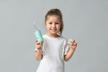 Cute little girl with oral irrigator and dental floss on grey background