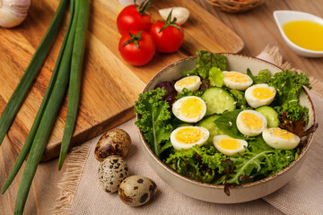 Bowl of tasty salad with boiled quail eggs and ingredients on wooden table