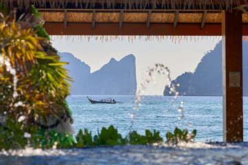 A landscape with a boat off the coast and green plants in the foreground. View from the pool